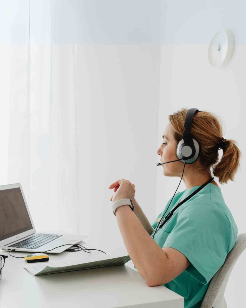 Female telepsychiatrist in green scrubs providing virtual mental health consultation using a laptop and headset